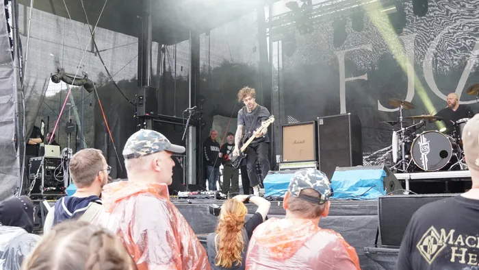Ein Musiker spielt E-Gitarre auf einer Außenbühne während eines Live-Auftritts vor einem Publikum.