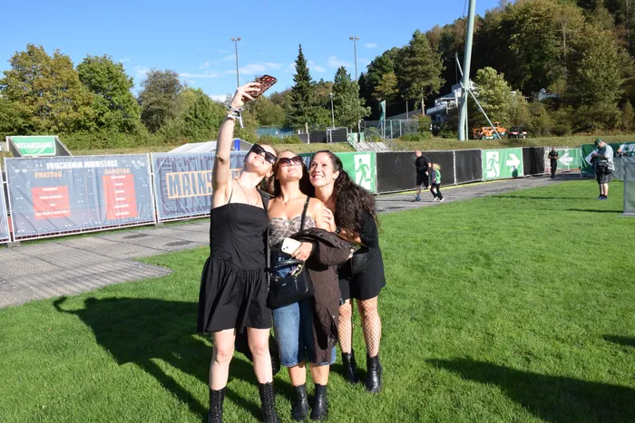 Drei junge Frauen posieren lächelnd für ein Selfie auf einer Wiese während des Bautz-Festivals.