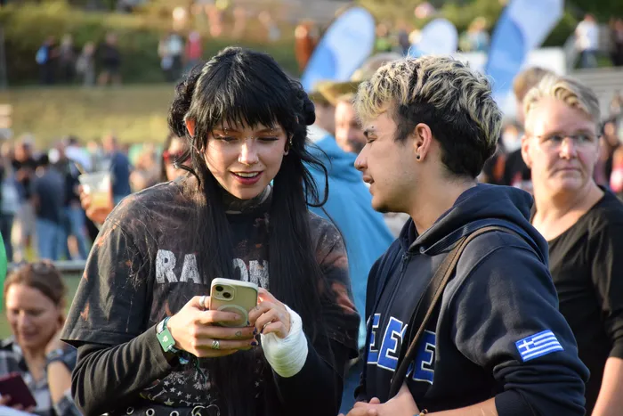 Zwei junge Menschen blicken in einer Menschenmenge gemeinsam auf das Display eines Smartphones.