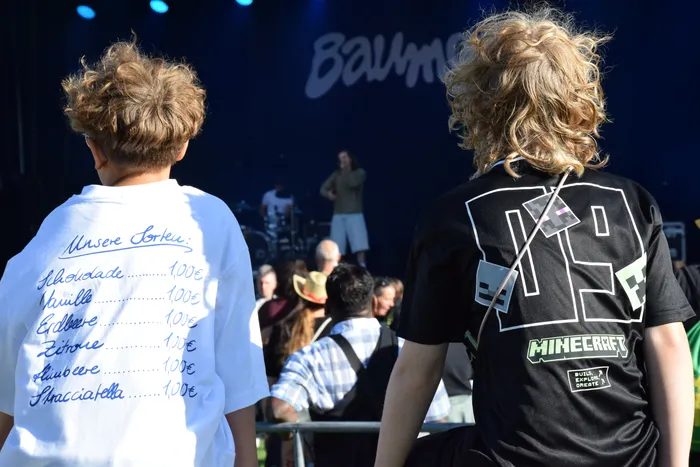 Zwei Besucher beim Bautz 2026: Eine Person trägt ein weißes T-Shirt mit einer handgeschriebenen Eissorten-Liste, die andere ein schwarzes Minecraft-Shirt.