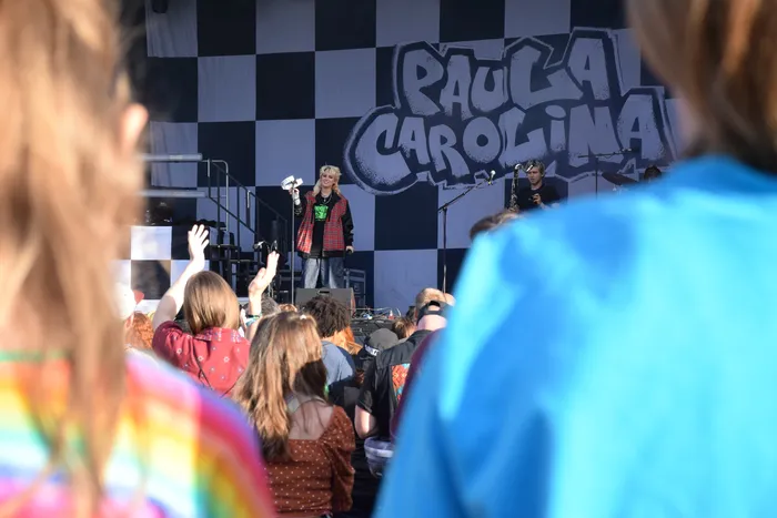 Sängerin der Band Paula Carolina auf einer Bühne vor einem schwarz-weiß karierten Hintergrund und einem Publikum.