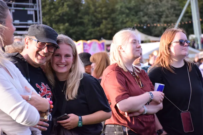 Lächelnde Menschen stehen in einer Menge bei einer Open-Air-Veranstaltung.
