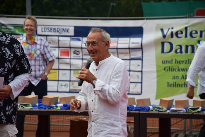 Ein lächelnder Mann mit Brille spricht in ein Mikrofon bei der Jubiläumsfeier der MTC/TC Halver Open.