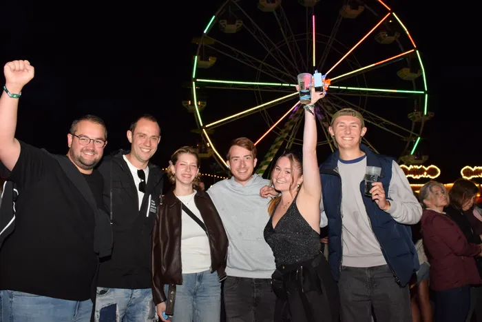 Eine Gruppe lachender Menschen posiert nachts vor einem bunt beleuchteten Riesenrad.