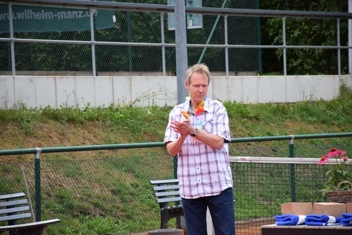 Ein Mann mit einer bunten Blumenkette klatscht bei der Jubiläumsfeier auf einer Tennisanlage.