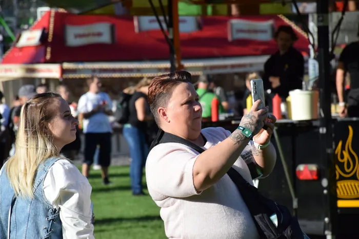 Eine Person fotografiert mit einem Smartphone bei einem sommerlichen Fest unter Sonnenschein.