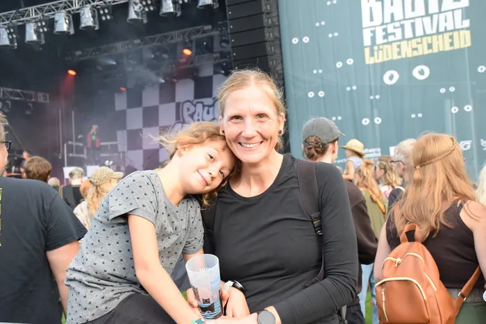 Eine lächelnde Frau und ein Mädchen lehnen sich eng aneinander, während sie im Publikum des Bautz Festivals in Lüdenscheid stehen.