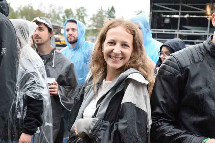 Eine lächelnde Frau mit langen, welligen Haaren steht in einer Menschenmenge mit Regenponchos.
