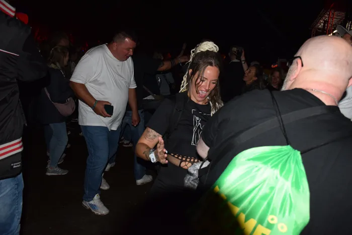 Eine lachende Frau mit blonden Dreadlocks tanzt in einer Menschenmenge bei einer nächtlichen Veranstaltung.