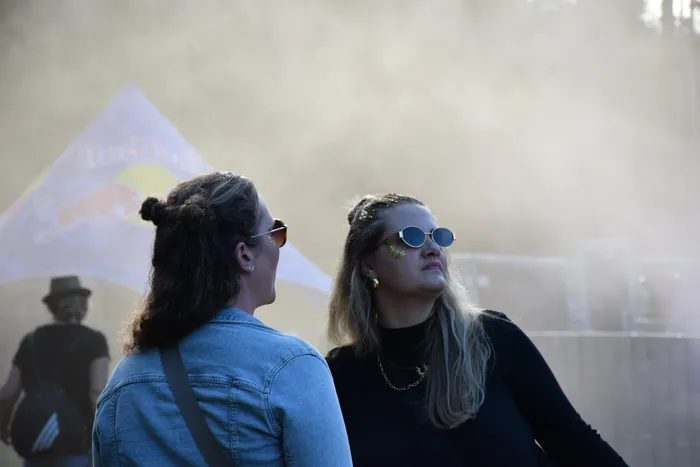 Zwei Personen blicken in eine staubige Umgebung bei einem Festival, im Hintergrund ist eine Red Bull Fahne zu sehen.