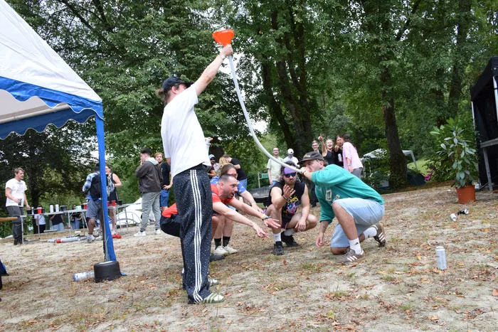 Ein Mann in weißem T-Shirt hält einen langen weißen Schlauch mit orangefarbenem Trichter hoch, während ein Mann in grünem T-Shirt davor kniet.