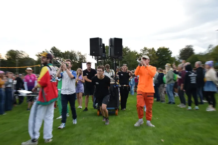 Eine Blaskapelle spielt mit Blasinstrumenten inmitten einer Menschenmenge auf einer Wiese.