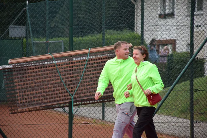 Ein Mann und eine Frau in neongrünen Kapuzenpullovern gehen lachend über einen Tennisplatz.
