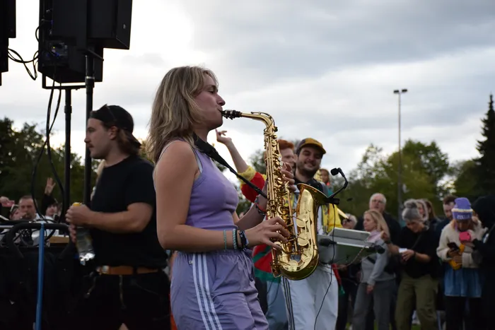 Eine junge Frau in einem lila Oberteil spielt Saxophon vor einer Menschenmenge im Freien.