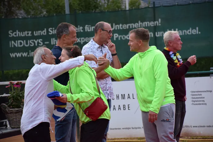 Ein Mann in einem weißen Hemd schüttelt einem Mann in einem neongrünen Hoodie die Hand bei der Jubiläumsfeier der MTC/TC Halver Open.