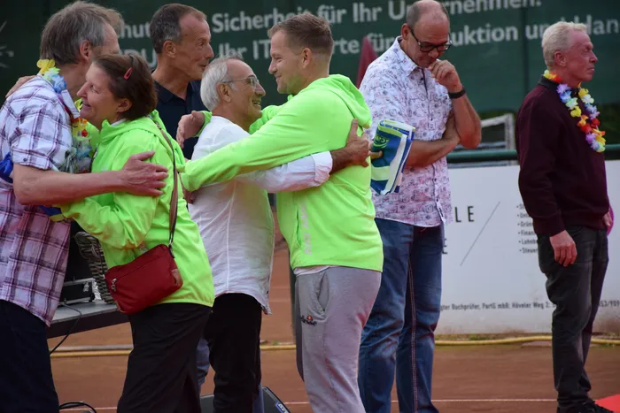 Mehrere Personen umarmen sich bei der Feier zum 20-jährigen Jubiläum der MTC/TC Halver Open auf einer Tennisanlage.