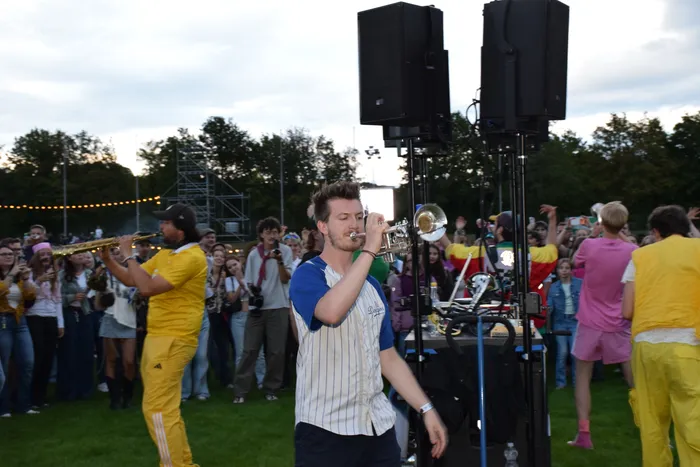 Ein Mann spielt Trompete inmitten einer Menschenmenge, während ein Musiker in gelber Kleidung Saxophon spielt.