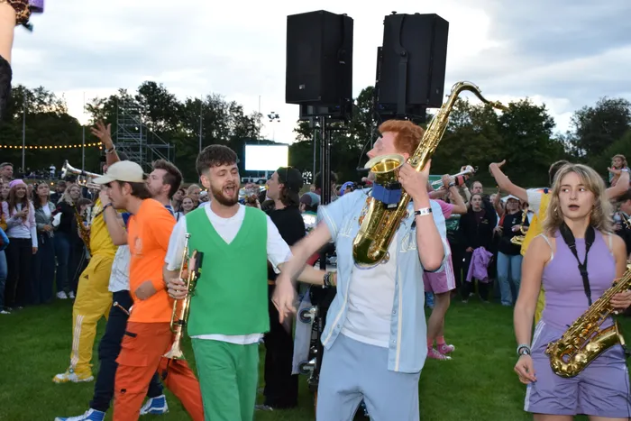 Musiker einer Blaskapelle spielen Saxophon und Trompete inmitten einer Menschenmenge im Freien.