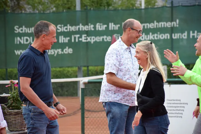 Menschen unterhalten sich lachend auf einem Tennisplatz während der Jubiläumsfeier der MTC/TC Halver Open.