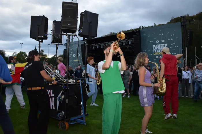 Musiker spielen Blasinstrumente wie Saxophone und Trompeten inmitten eines Publikums vor einer Bühne mit der Aufschrift „BAUTZ FESTIVAL“.