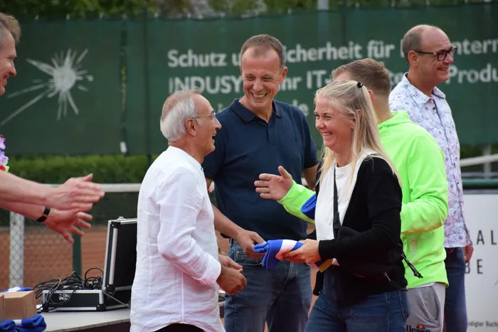 Eine Gruppe lachender Menschen feiert das 20-jährige Jubiläum der MTC/TC Halver Open auf einer Tennisanlage.