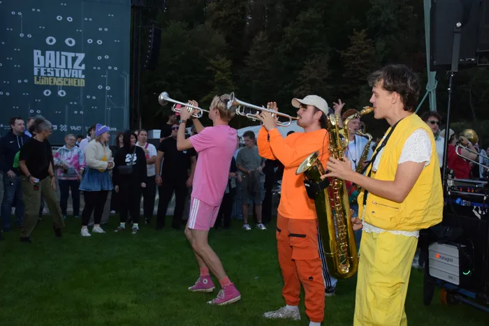 Musiker in farbenfroher Kleidung spielen Trompete und Saxophon vor einem Publikum beim Baltz Festival.