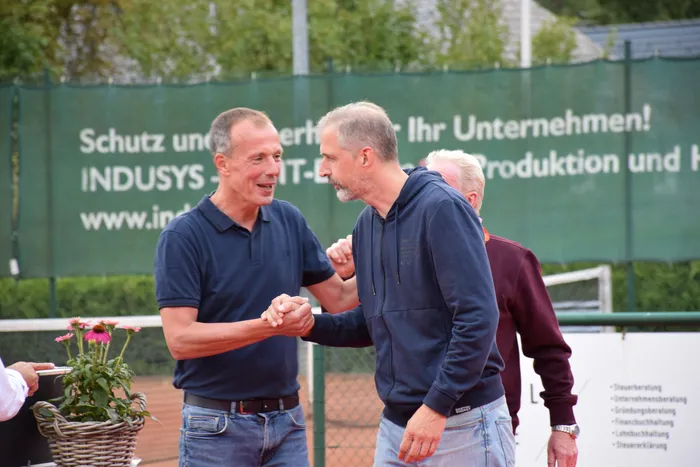 Zwei Männer schütteln sich auf einem Tennisplatz die Hände.