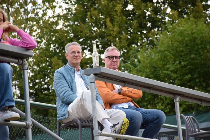 Zwei Männer sitzen auf einer Tribüne bei der MTC/TC Halver Open vor einer Kulisse aus grünen Bäumen.