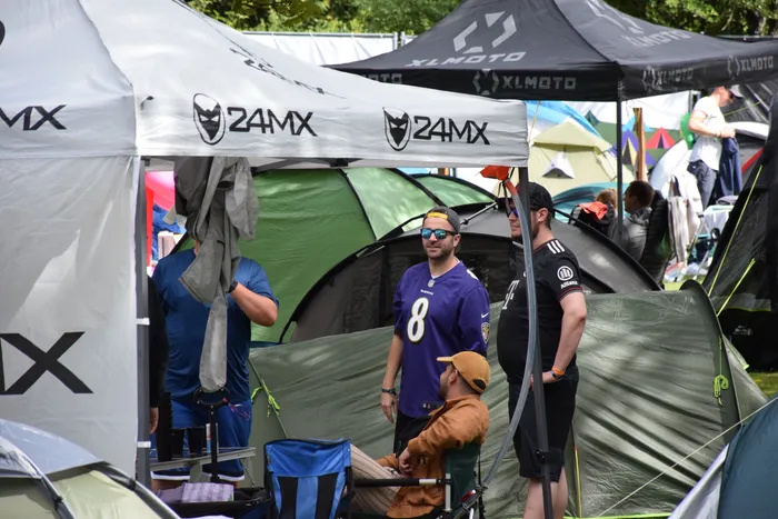 Menschen stehen zwischen Zelten bei einem Event, darunter ein lächelnder Mann in einem lila Trikot mit der Nummer 8.