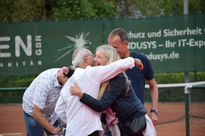 Eine Gruppe von Menschen umarmt sich auf einem Tennisplatz während der Jubiläumsfeier.