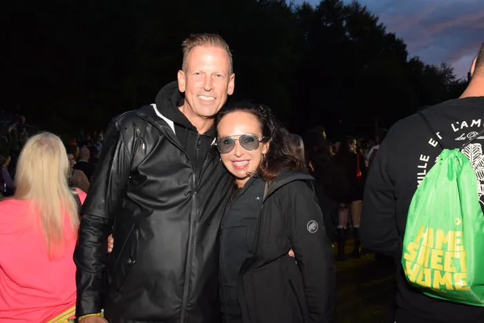 Ein Mann und eine Frau in schwarzen Jacken lächeln gemeinsam bei einer Abendveranstaltung im Freien.