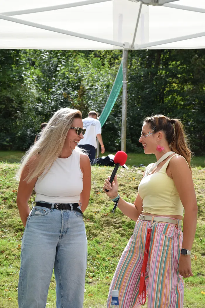 Eine Frau mit einem roten Mikrofon interviewt eine lächelnde Frau unter einem weißen Zelt im Freien.