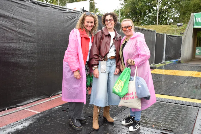 Drei lächelnde Frauen in bunten Regenmänteln stehen auf einer nassen Fläche beim Bautz-Samstag.