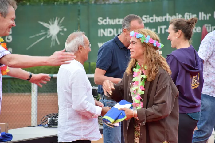 Eine Frau mit Blumenkranz und Lei-Kette lacht im Gespräch mit einem Mann bei der Jubiläumsfeier der MTC/TC Halver Open.