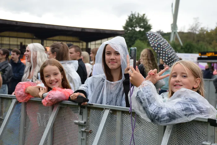 Junge Menschen in transparenten Regenponchos lächeln hinter einer Metallabsperrung beim Bautz-Samstag.