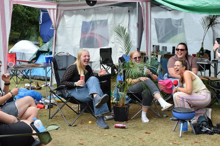Lachende junge Frauen sitzen in Campingstühlen vor Zelten beim Bautz Samstag 2026.
