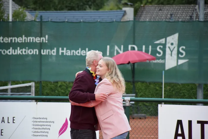 Ein Mann mit bunter Blumenkette und eine Frau in einem rosa Blazer umarmen sich bei der Jubiläumsfeier der MTC/TC Halver Open.