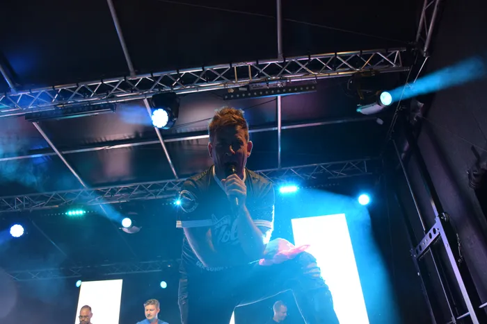 Almklausi singt mit einem Mikrofon auf einer Bühne unter blauem Scheinwerferlicht.