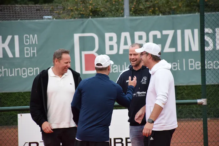 Vier Männer stehen im Gespräch auf einem Tennisplatz vor einem grünen Banner.