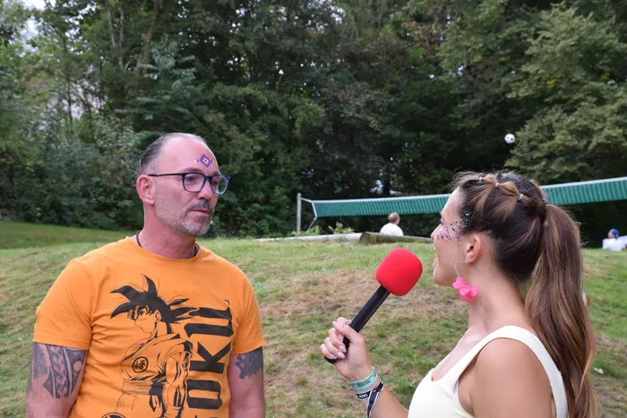 Eine Frau mit Glitzer im Gesicht interviewt einen Mann in einem orangefarbenen T-Shirt mit Anime-Aufdruck im Freien.