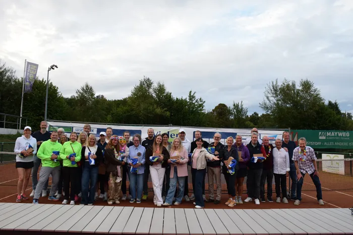 Eine Gruppe von Menschen posiert mit Trophäen für ein Gruppenfoto zum 20-jährigen Jubiläum der MTC/TC Halver Open auf einer Tennisanlage.