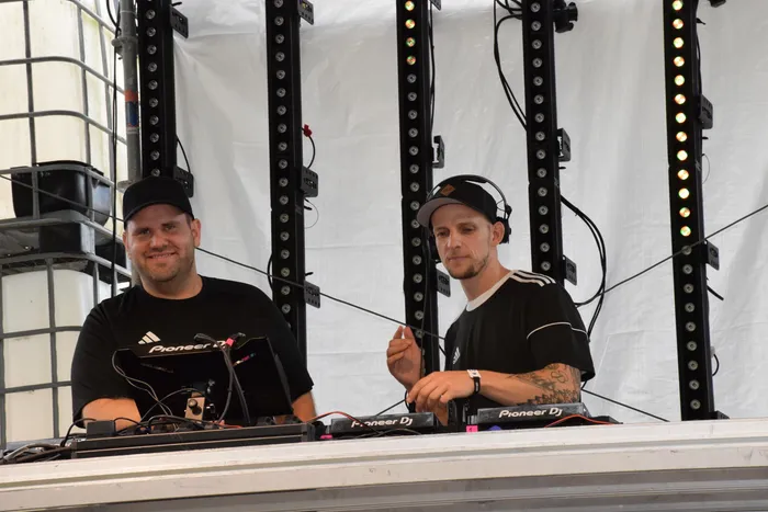 Zwei DJs an einem Mischpult mit Pioneer-Equipment vor vertikalen Lichtleisten auf einer Bühne.