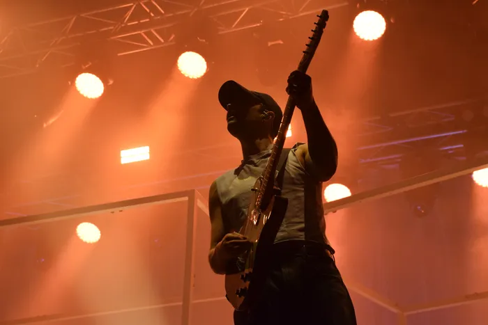 Silhouette eines Musikers beim Spielen einer E-Gitarre vor hellen, orangefarbenen Bühnenlichtern.