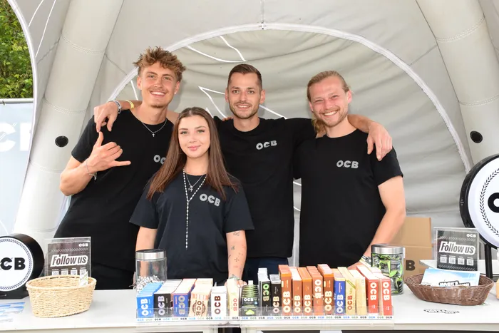 Vier lächelnde Personen in schwarzen OCB-T-Shirts stehen hinter einem Tisch mit verschiedenen OCB-Produkten unter einem weißen Zelt.