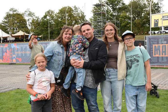 Eine Gruppe von fünf Personen, zwei Erwachsene und drei Kinder, lächelt gemeinsam bei einer Veranstaltung im Freien.