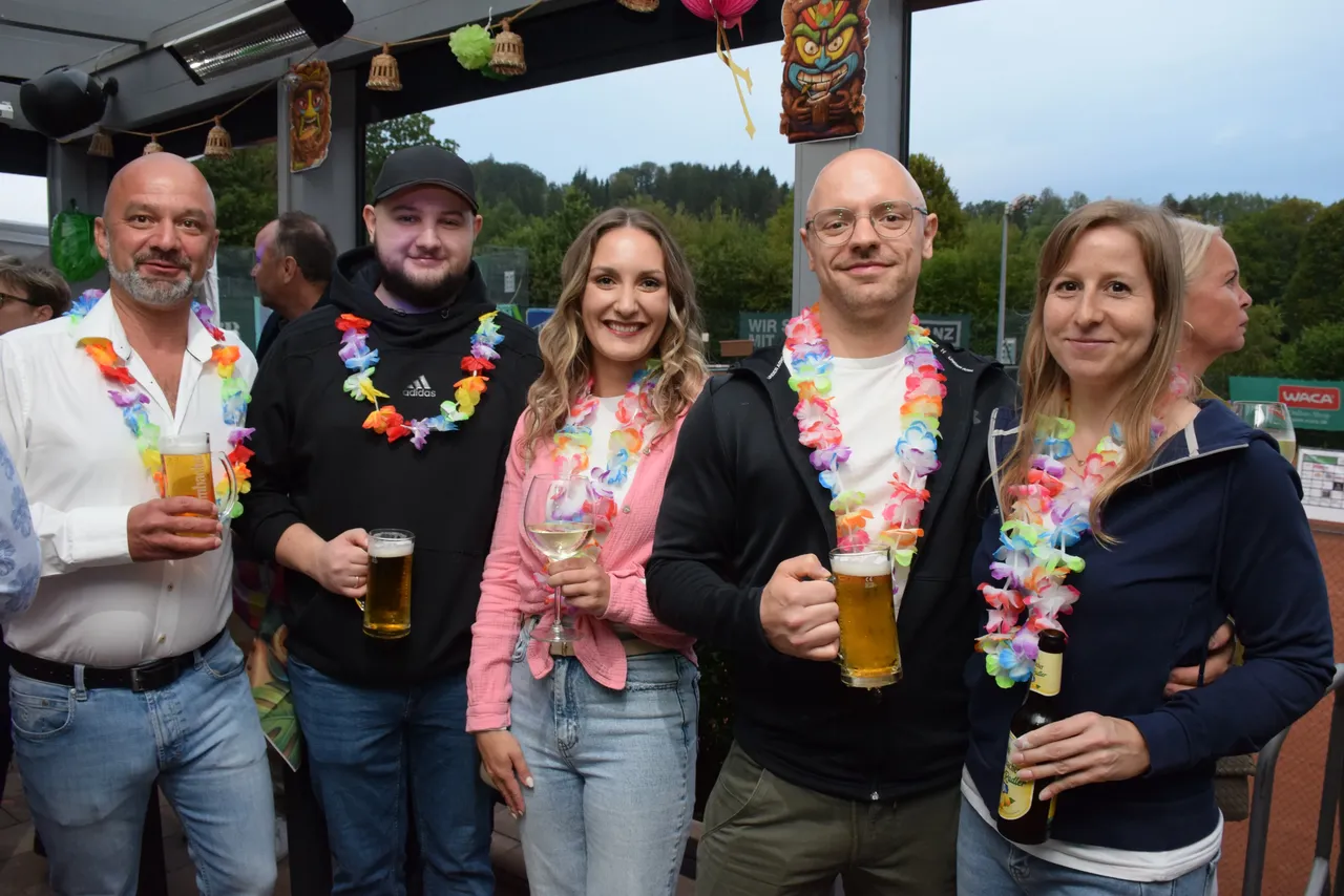 Fünf lächelnde Personen mit bunten Blumenketten halten Getränke und feiern das Jubiläum der MTC/TC Halver Open.