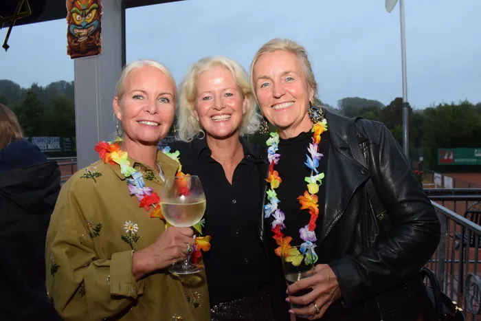 Drei lächelnde Frauen mit bunten Blumenketten und Getränken feiern das 20-jährige Jubiläum der MTC/TC Halver Open.