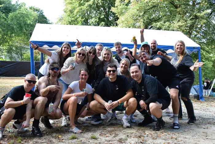 Eine Gruppe lachender Menschen posiert vor einem weißen Zelt auf einem Campingplatz.