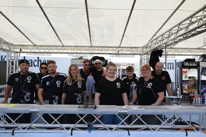 Eine Gruppe von Menschen in schwarzen T-Shirts steht hinter einem Tresen unter einem Festzelt auf dem Bautz-Festival.