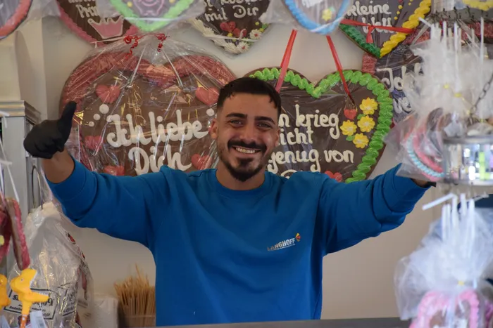 Ein lächelnder Mann in einem blauen Sweatshirt gibt ein Daumen-hoch-Zeichen vor verzierten Lebkuchenherzen.